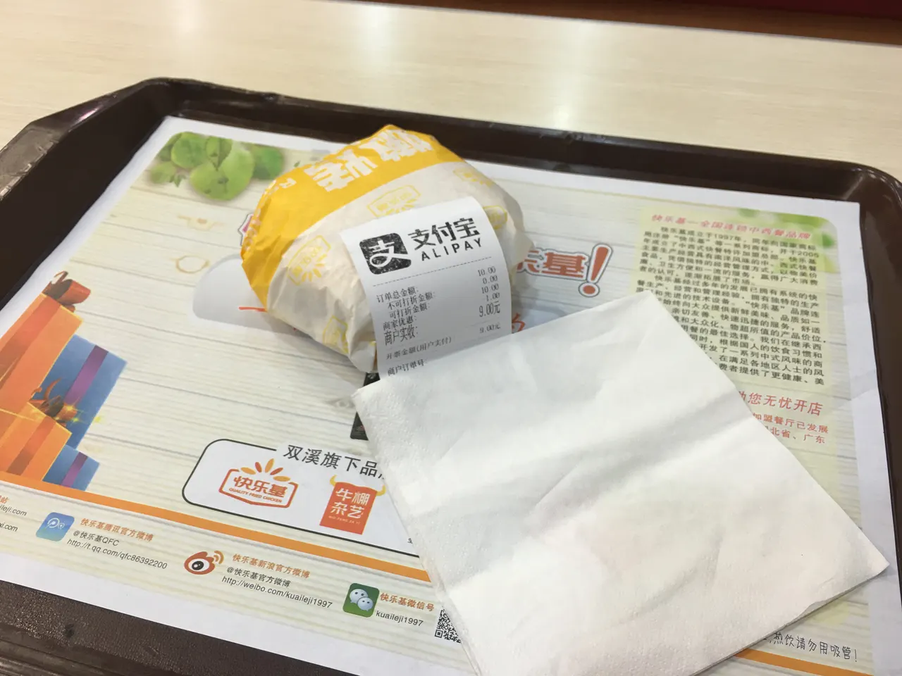 Recibo de pago de Alipay en una bandeja junto a una hamburguesa envuelta