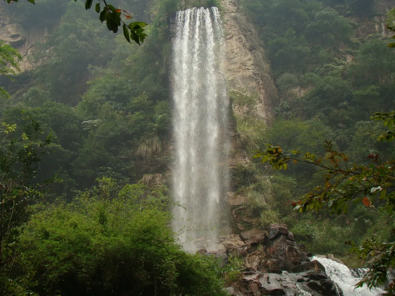 La cascata di Baofeng scende lungo una parete rocciosa verso un torrente nel bosco