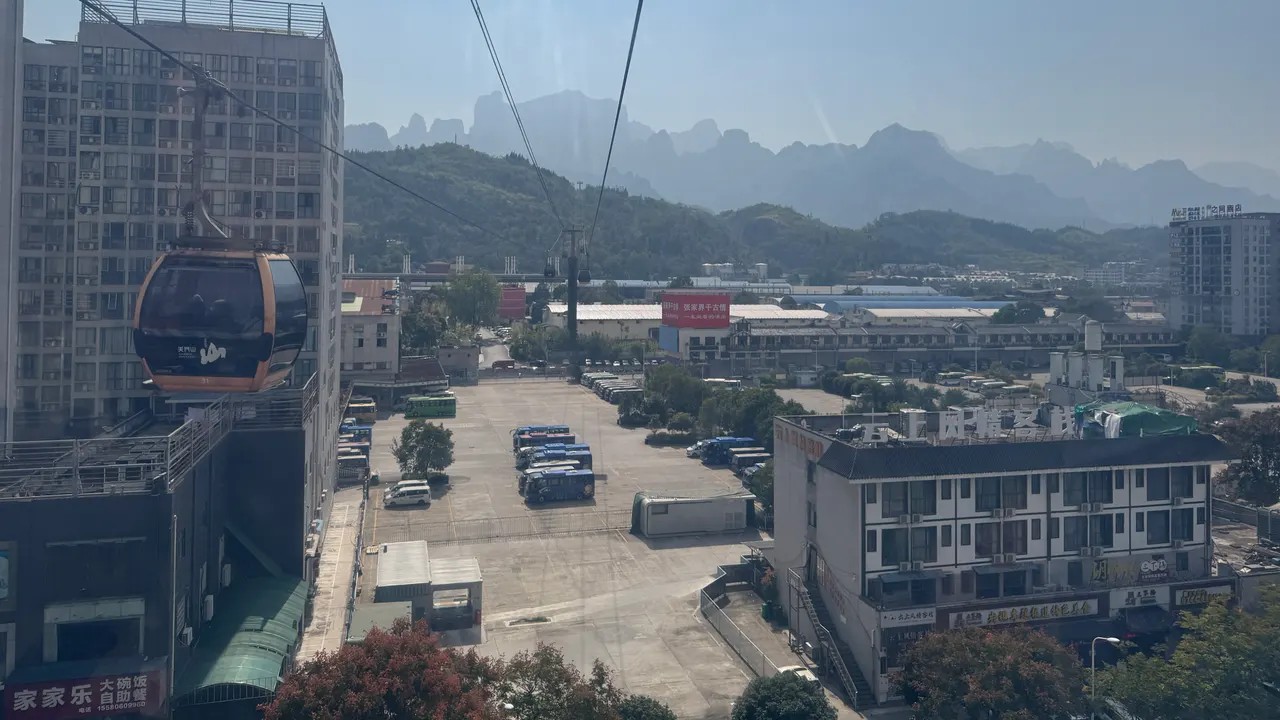Autobus nel piazzale della stazione centrale di Zhangjiajie, con l’edificio del terminal e una cabina della funivia di Tianmen