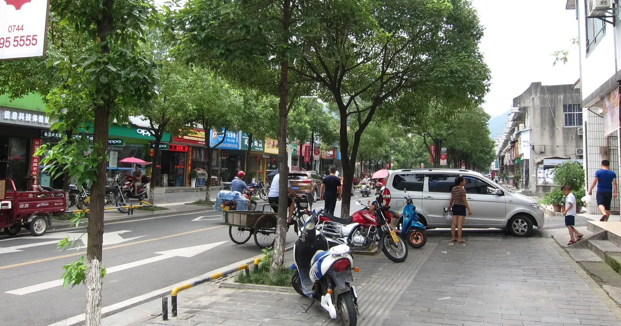 Personas, motos aparcadas y tiendas junto a una calle arbolada de Wulingyuan