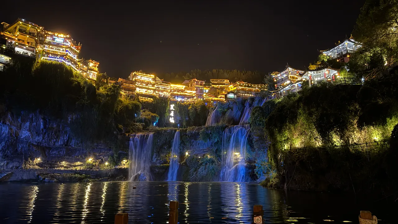 Cascada iluminada de Furong, casas junto al acantilado y reflejos en el agua