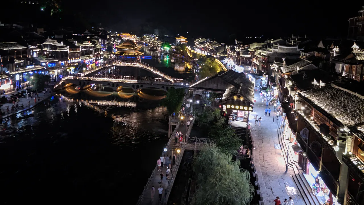 Ponte e case illuminati sul fiume Tuojiang a Fenghuang, con riflessi sull’acqua
