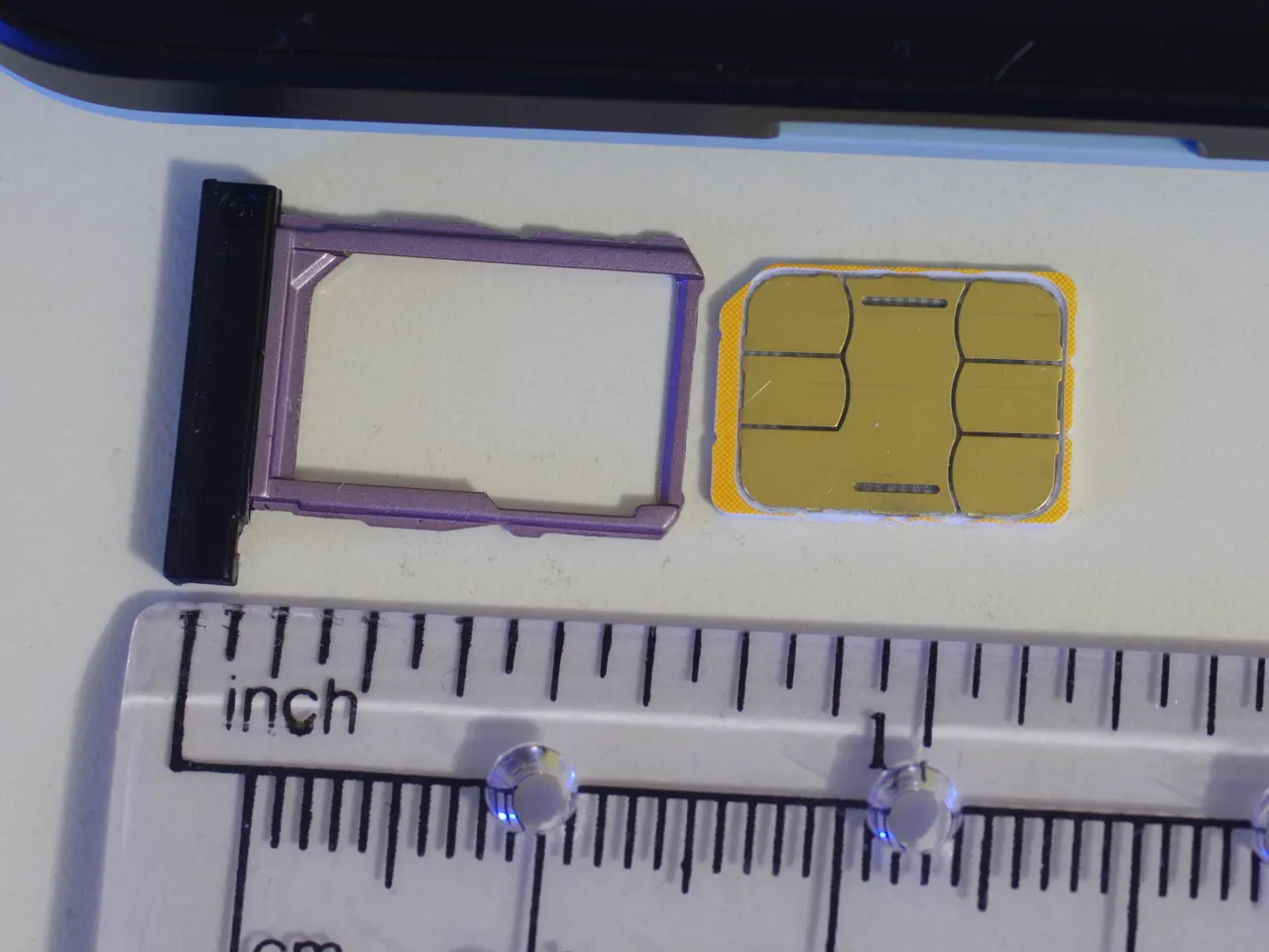 Tarjeta nano-SIM y su bandeja junto a un teléfono, con una regla que muestra su tamaño