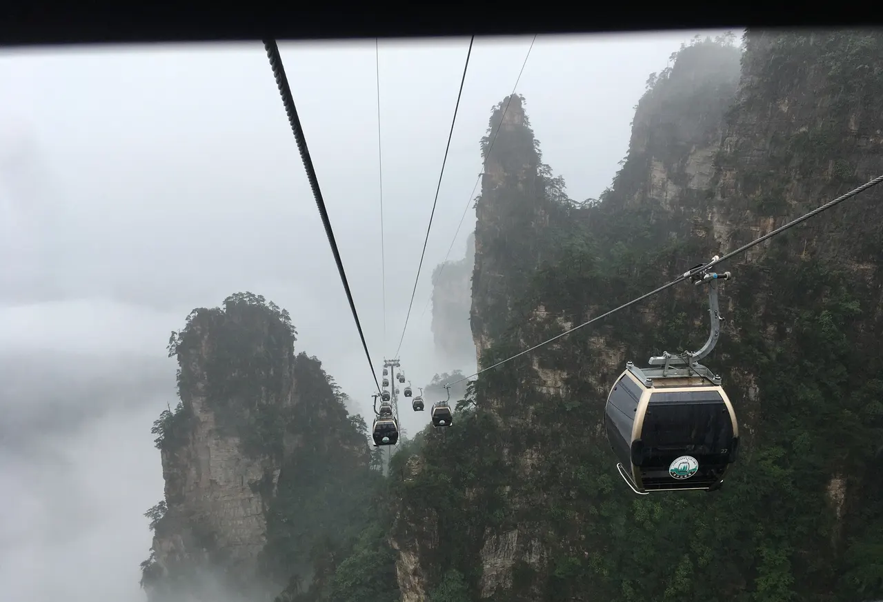 Cabine della funivia Tianzi tra pilastri rocciosi boscosi nella nebbia, viste da un’altra cabina