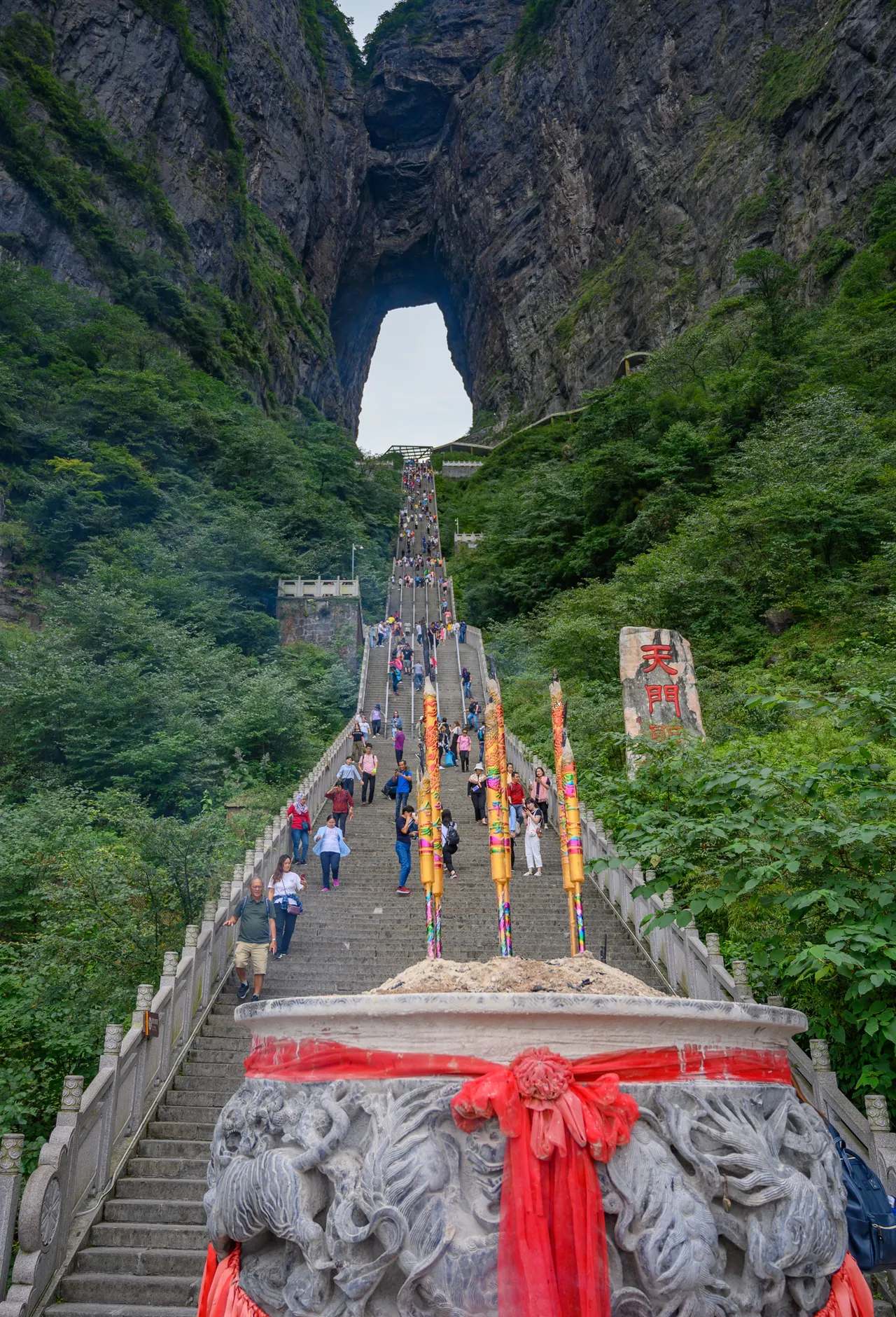 Visitantes en la escalera bajo la cueva de Tianmen y un incensario delante