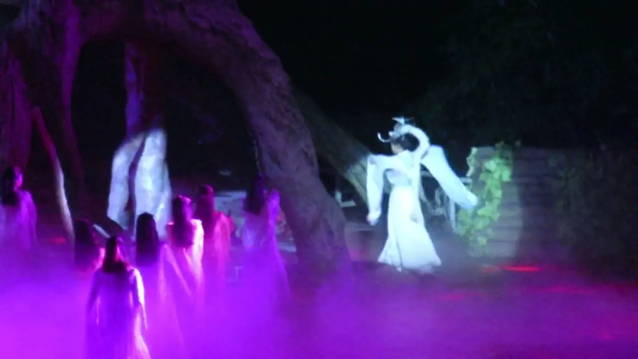 Artistas vestidos de blanco y rosa en el escenario de roca de Hada Zorro de Tianmen bajo luces violetas