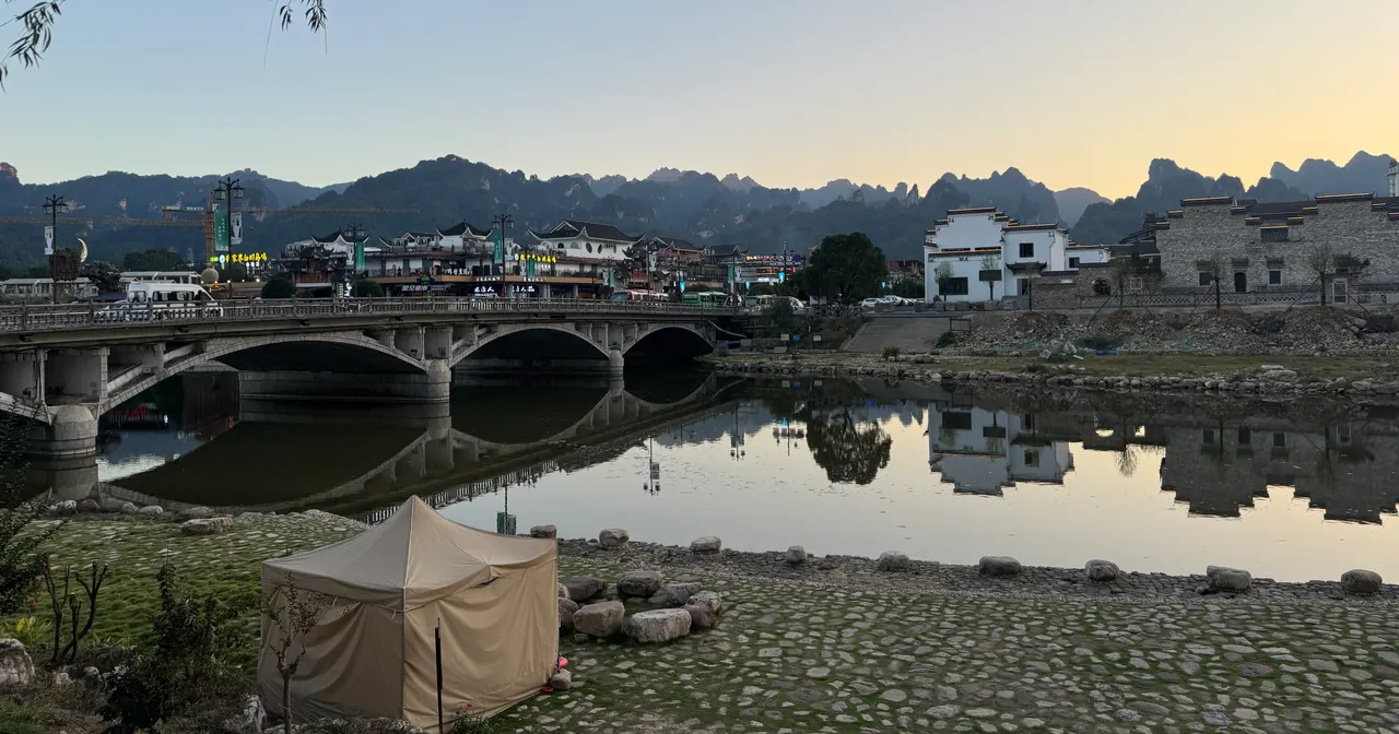 Ponte ad archi in pietra, edifici lungo il fiume e montagne a Wulingyuan al crepuscolo