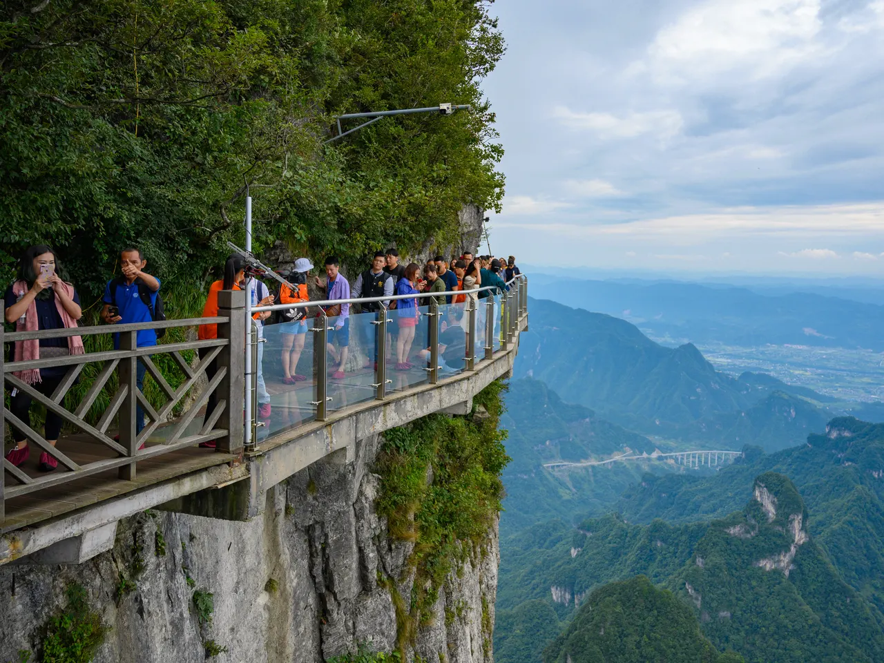 Visitatori con borse piccole e copriscarpe sulla passerella di vetro del monte Tianmen