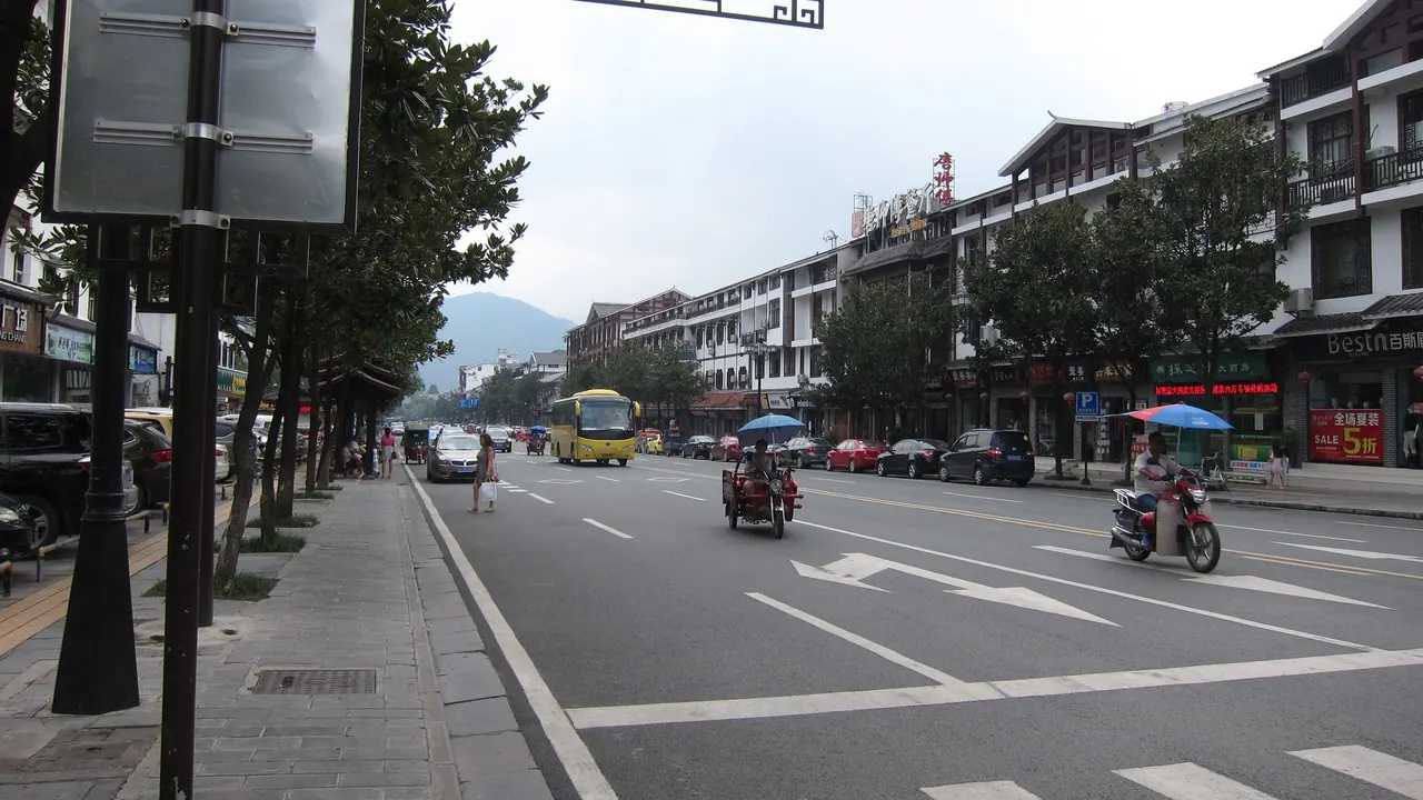 Una calle de Wulingyuan con acera, tiendas y montañas en 2016